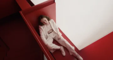 From photograph to visual fiction: directing images with AI Overhead portrait of a person in a white suit sitting in a geometric architectural space with intense red walls and diffuse light, exemplifying art direction and AI-assisted visual fiction.