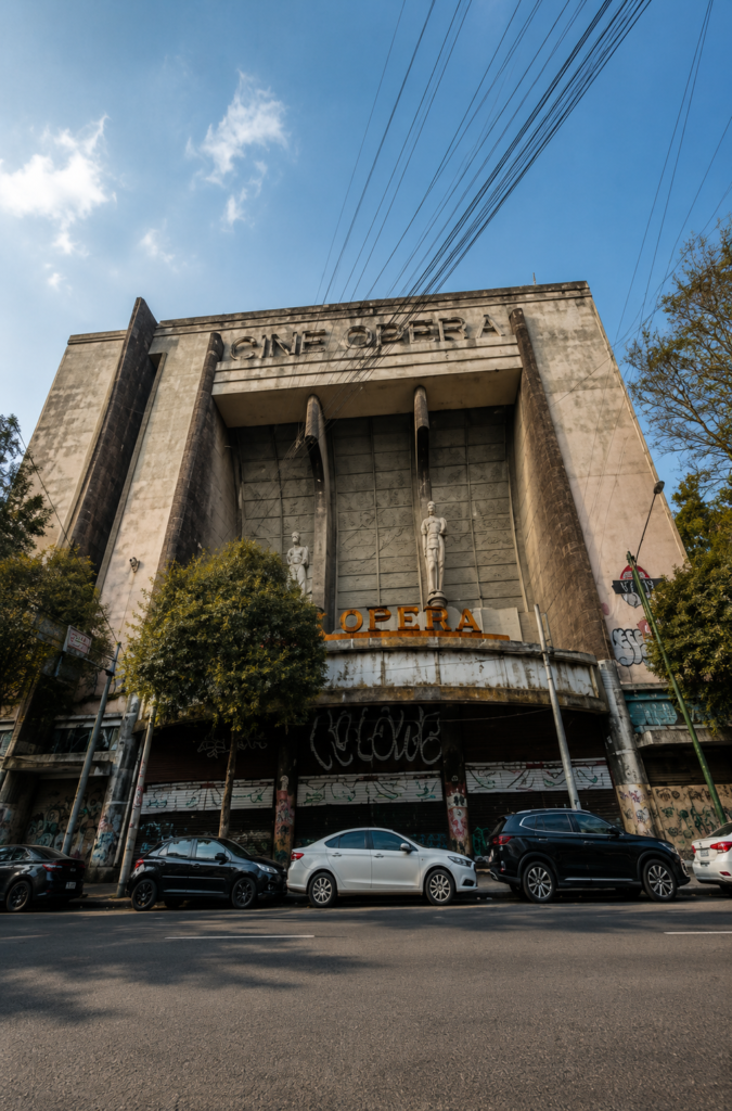 Vista exterior en ángulo contrapicado de la imponente fachada Art Decó abandonada del antiguo Cine Ópera con sus dos majestuosas esculturas de piedra, en la colonia San Rafael de la Ciudad de México.