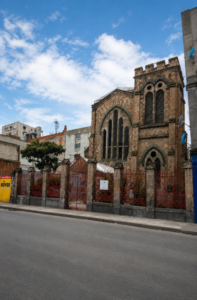 Fachada de estilo neogótico inglés de la Antigua Christ Church (Museo Británico Americano) en la calle Artículo 123 de la Ciudad de México, mostrando sus ventanas ojivales apuntadas y su torre almenada de piedra dañada bajo un cielo parcialmente nublado.