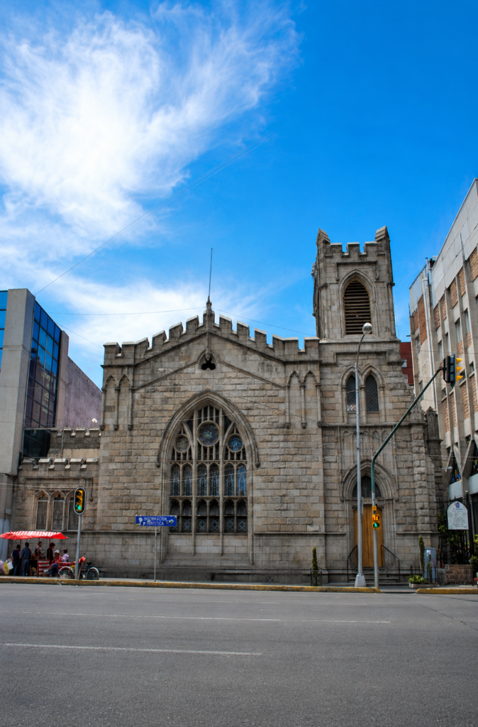 Fachada de piedra de la Iglesia Metodista El Mesías en la Avenida Balderas, Ciudad de México, mostrando su arquitectura neogótica con gran vitral ojival y torre campanario bajo un cielo azul.