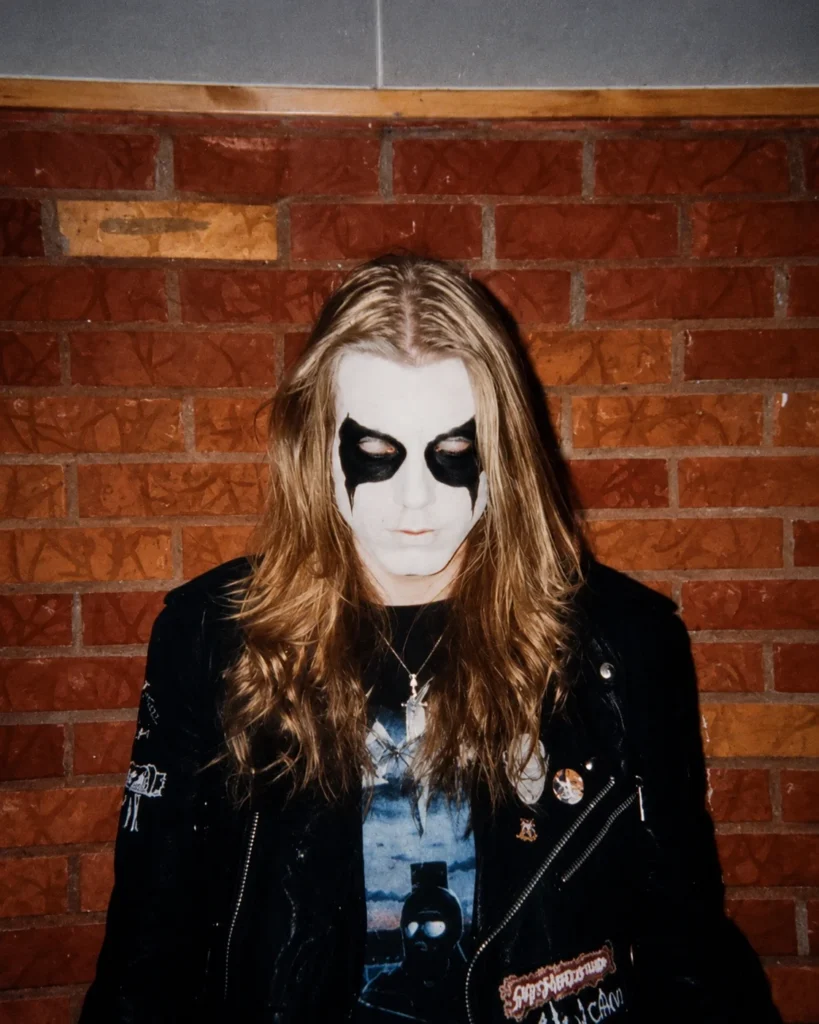 Retrato de Dead, vocalista de Mayhem, luciendo su icónico corpse paint sobre un fondo de pared de ladrillos.