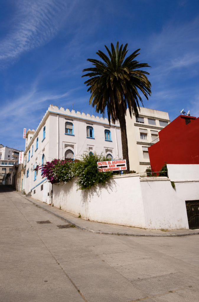 Fachada blanca del Hotel El Muniria en Tánger, Marruecos, con ventanas azules, bugambilias y una palmera, lugar donde William S. Burroughs escribió El almuerzo desnudo.