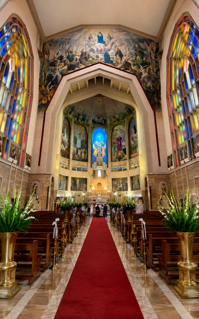 Interior de la Parroquia del Purísimo Corazón de María en CDMX, mostrando el pasillo central con alfombra roja, vitrales monumentales de colores y murales religiosos de estilo neogótico moderno.