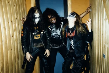 Tres músicos de Mayhem con maquillaje corpse paint y chamarras de piel posando en backstage.
