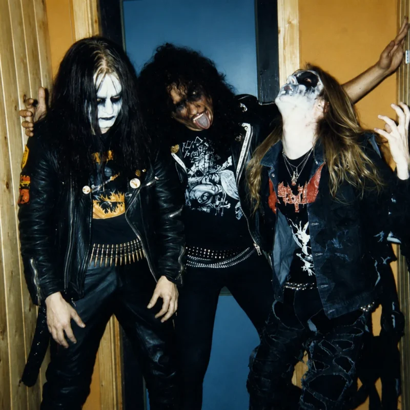 Tres músicos de Mayhem con maquillaje corpse paint y chamarras de piel posando en backstage.