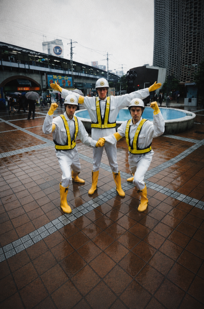 Adam Horovitz (Ad-Rock), Michael Diamond (Mike D) y Adam Yauch (MCA) de la banda Beastie Boys, posando frente a una fuente en Tokio, Japón, con trajes blancos, chalecos reflectantes amarillos y cascos de obreros de la construcción durante el rodaje del video musical Intergalactic en junio de 1998.