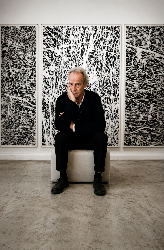 Retrato a color del artista neerlandés Jan Hendrix sentado en su estudio frente a un gran tríptico de grabados abstractos en blanco y negro.
