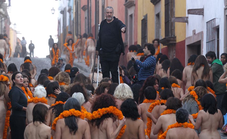 El fotógrafo Spencer Tunick de pie sobre una escalera de aluminio dirigiendo a decenas de mujeres desnudas que llevan guirnaldas de flores de cempasúchil en el cuello, durante la instalación Sendero de los Redimidos en San Miguel de Allende.