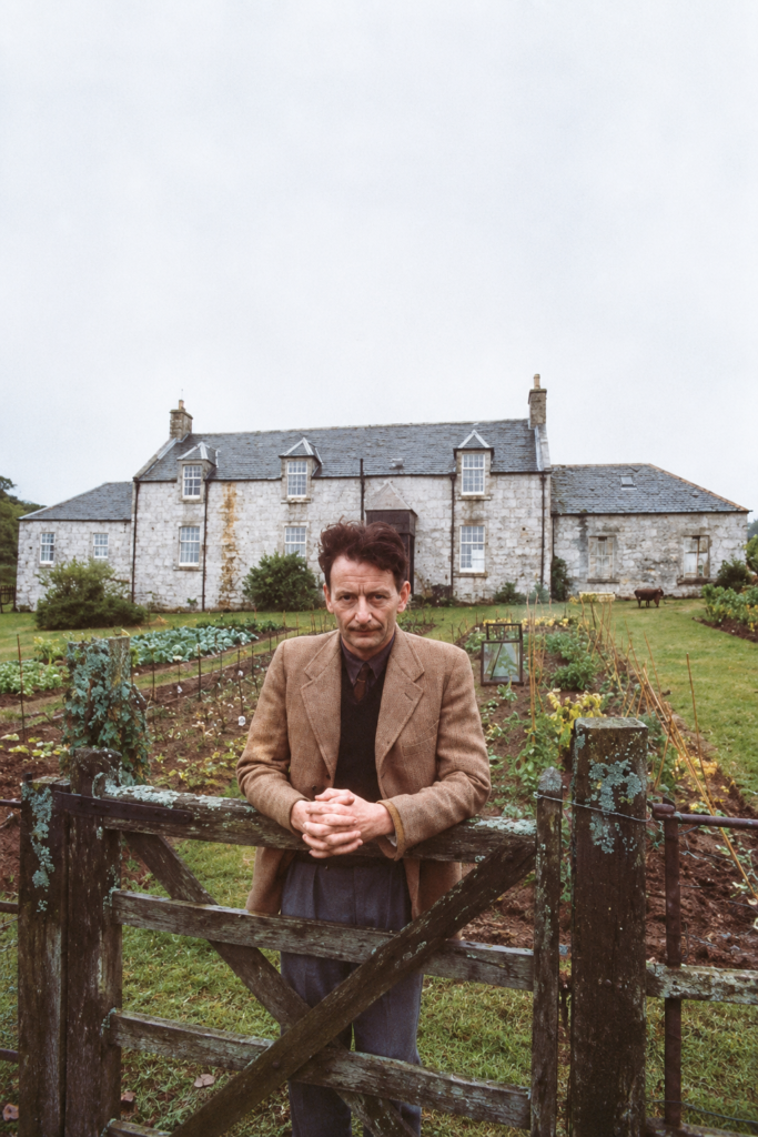 George Orwell posa apoyado en una valla de madera frente a su remota granja de Barnhill en la isla de Jura, Escocia, donde escribió la novela 1984.