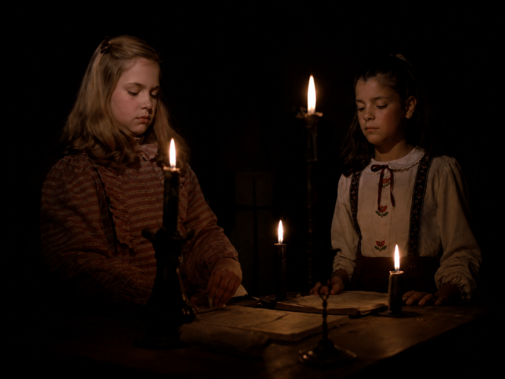 Fotograma oscuro de la película mexicana Veneno para las hadas con Verónica y Flavia sentadas a la mesa leyendo un libro de brujería iluminadas por velas, anunciando el concierto y proyección en vivo en Casa del Lago UNAM, México.