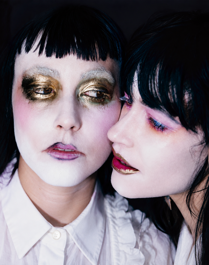 Bianca y Sierra Casady de CocoRosie posan con maquillaje teatral blanco, dorado y rosa en un retrato promocional.