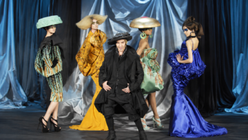 Cómo entender una colección de John Galliano: las referencias históricas, literarias y cinematográficas detrás de su obra John Galliano posa rodeado de modelos con vestidos escultóricos y sombreros teatrales durante un desfile de alta costura.