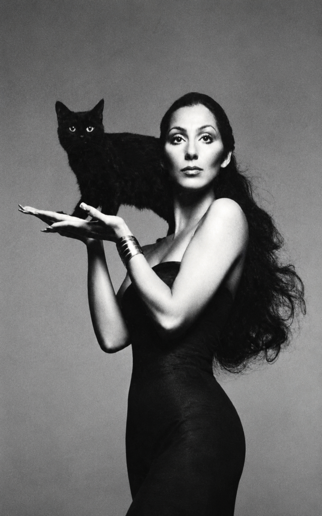 Mujer con vestido negro sostiene un gato negro en un retrato de Richard Avedon de 1974 asociado con misterio y sensualidad felina.