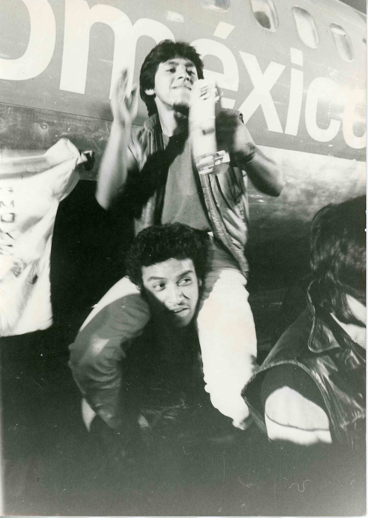 Jóvenes en una escena de concierto de ¿Cómo ves?, de Paul Leduc; uno sobre los hombros de otro, frente al fuselaje de un avión.