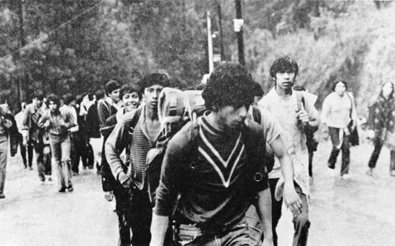 Jóvenes con mochilas caminan por una carretera rumbo al festival de Avándaro de 1971, en una fotografía en blanco y negro.