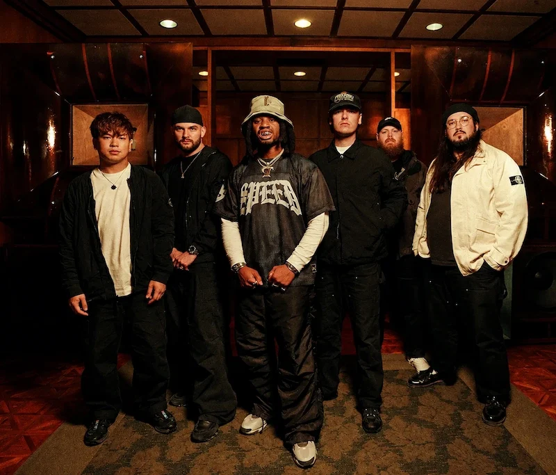 Knocked Loose y Denzel Curry posan juntos en un interior con paneles de madera y grandes altavoces.