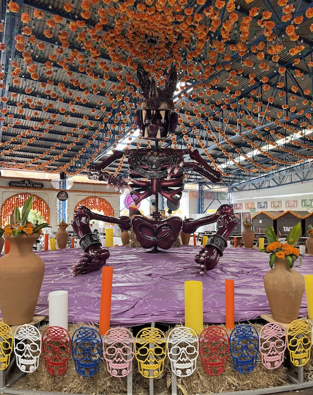 Figura esquelética monumental bajo un techo de flores naranjas, entre vasijas y calaveras multicolores, en el Valle de Catrinas de Atlixco.