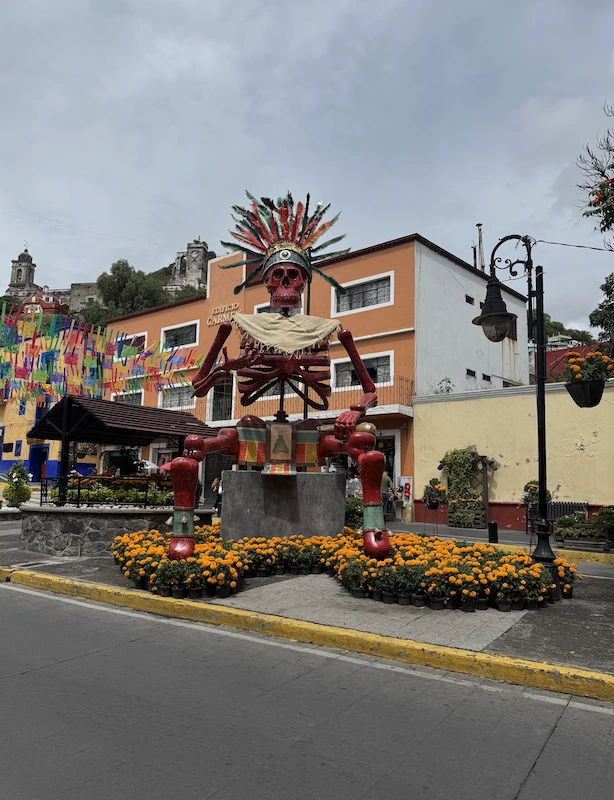 Catrina monumental roja con penacho multicolor, sentada y rodeada de cempasúchil en el Valle de Catrinas de Atlixco, Puebla.